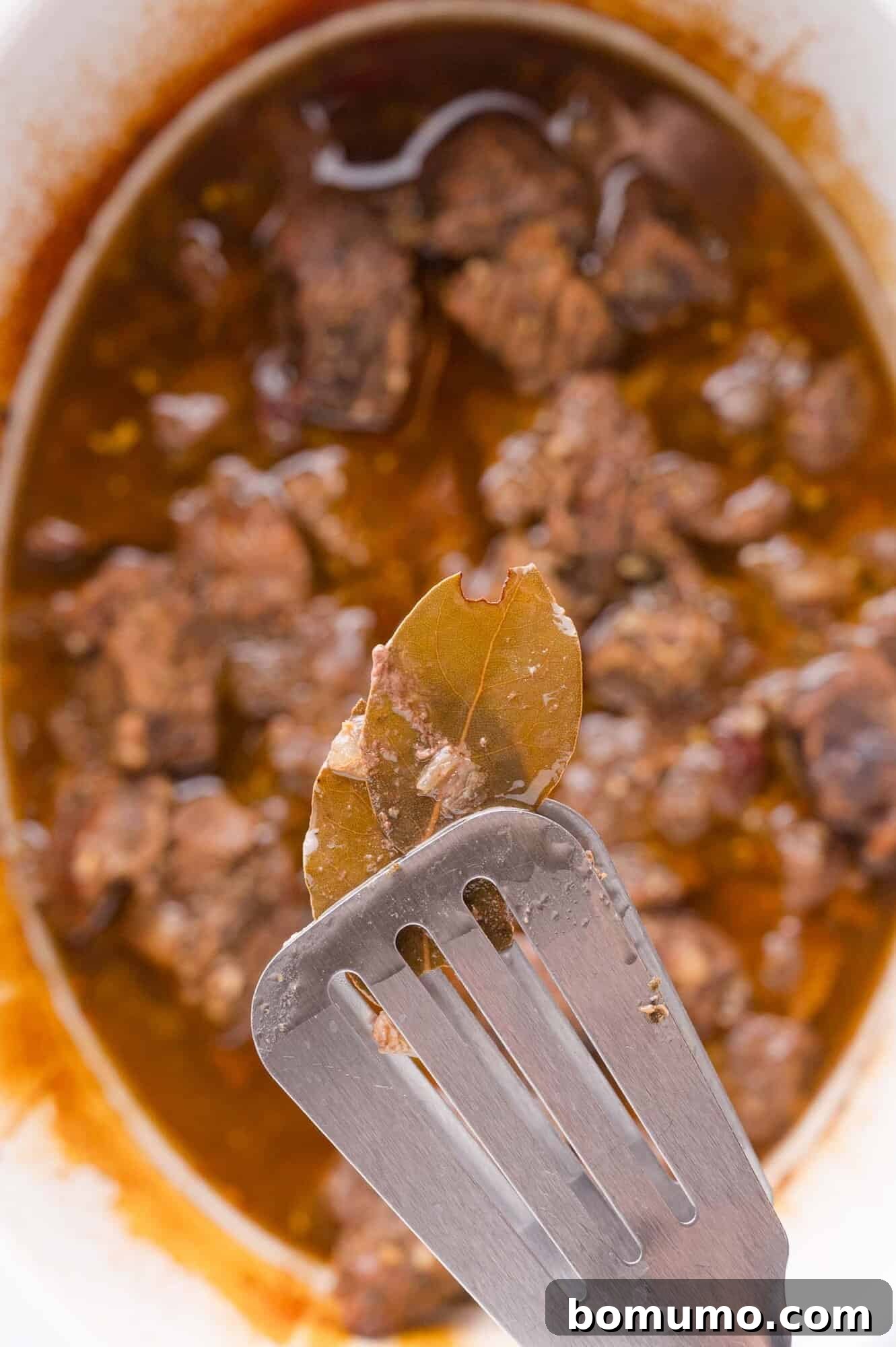 Effortless Shredded Barbacoa 10 Removing a bay leaf from the cooked barbacoa beef in the slow cooker.