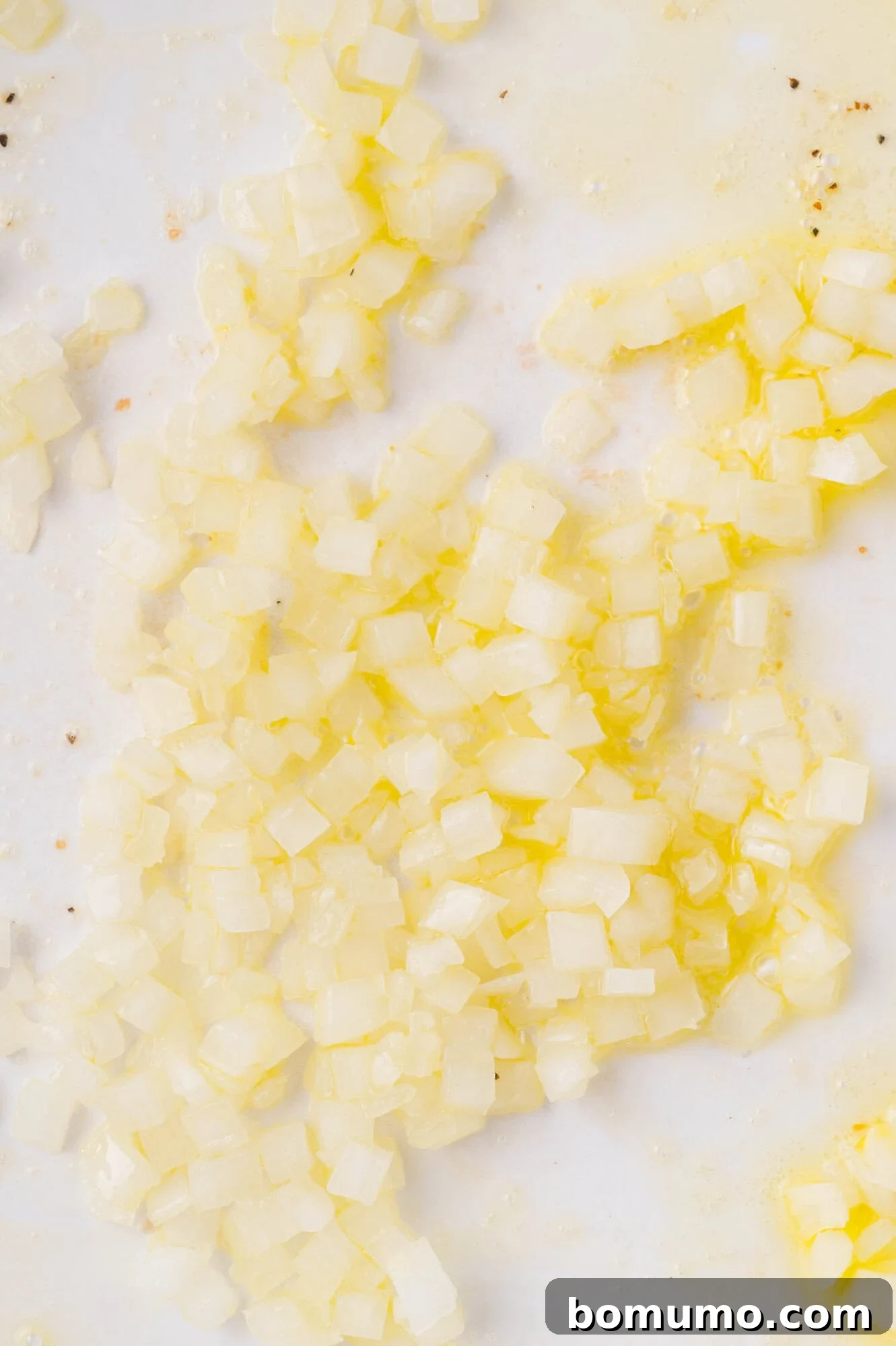 Diced onions being sautéed in oil in a white pan, with some pieces appearing translucent.