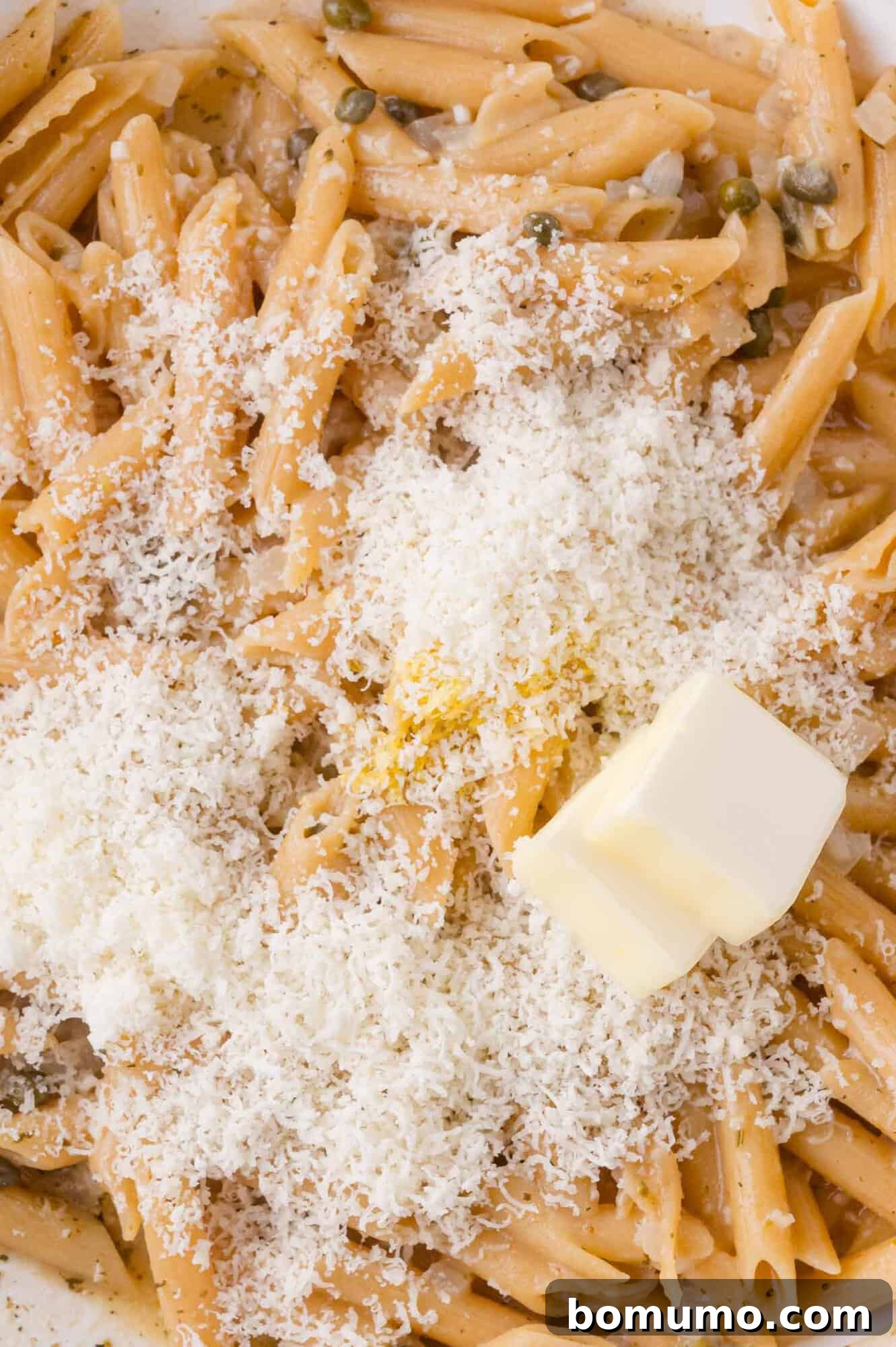 Close-up of cooked penne pasta topped with grated cheese and a pat of butter.