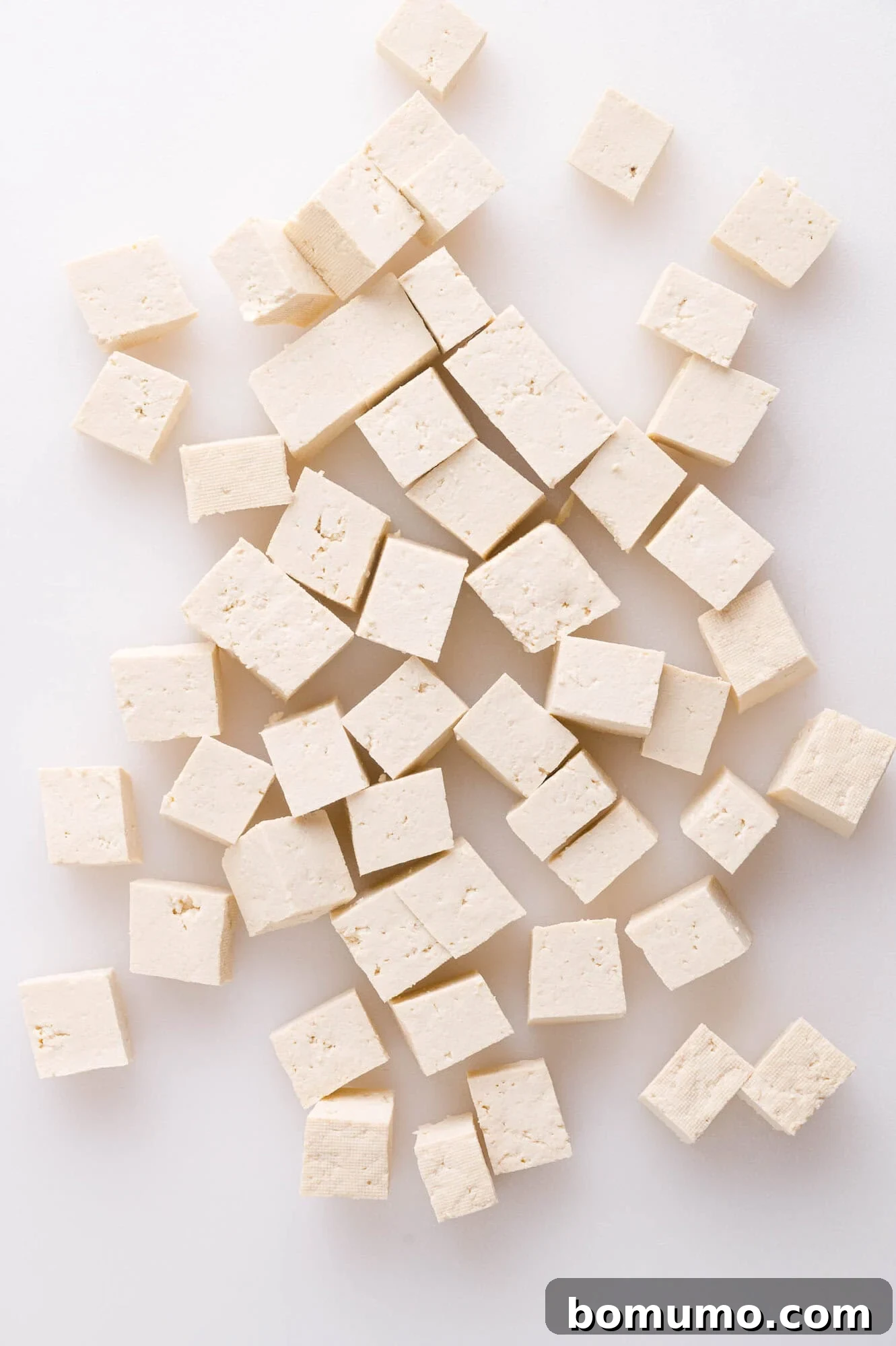 Cubed pieces of firm tofu scattered on a white surface.
