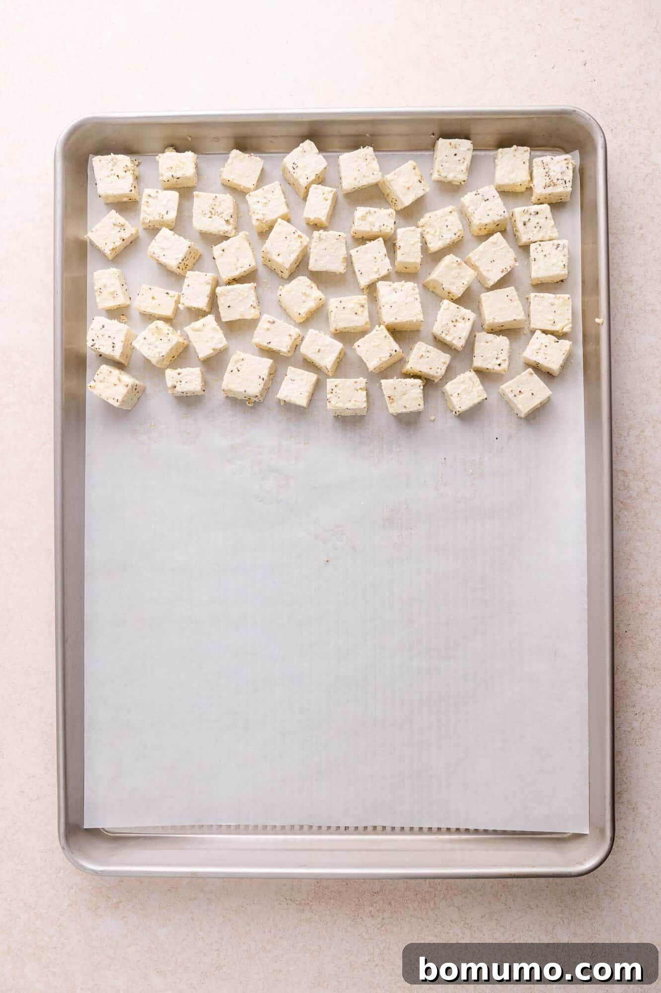Cubes of seasoned tofu are arranged in a single layer on a parchment-lined baking sheet, ready for roasting.