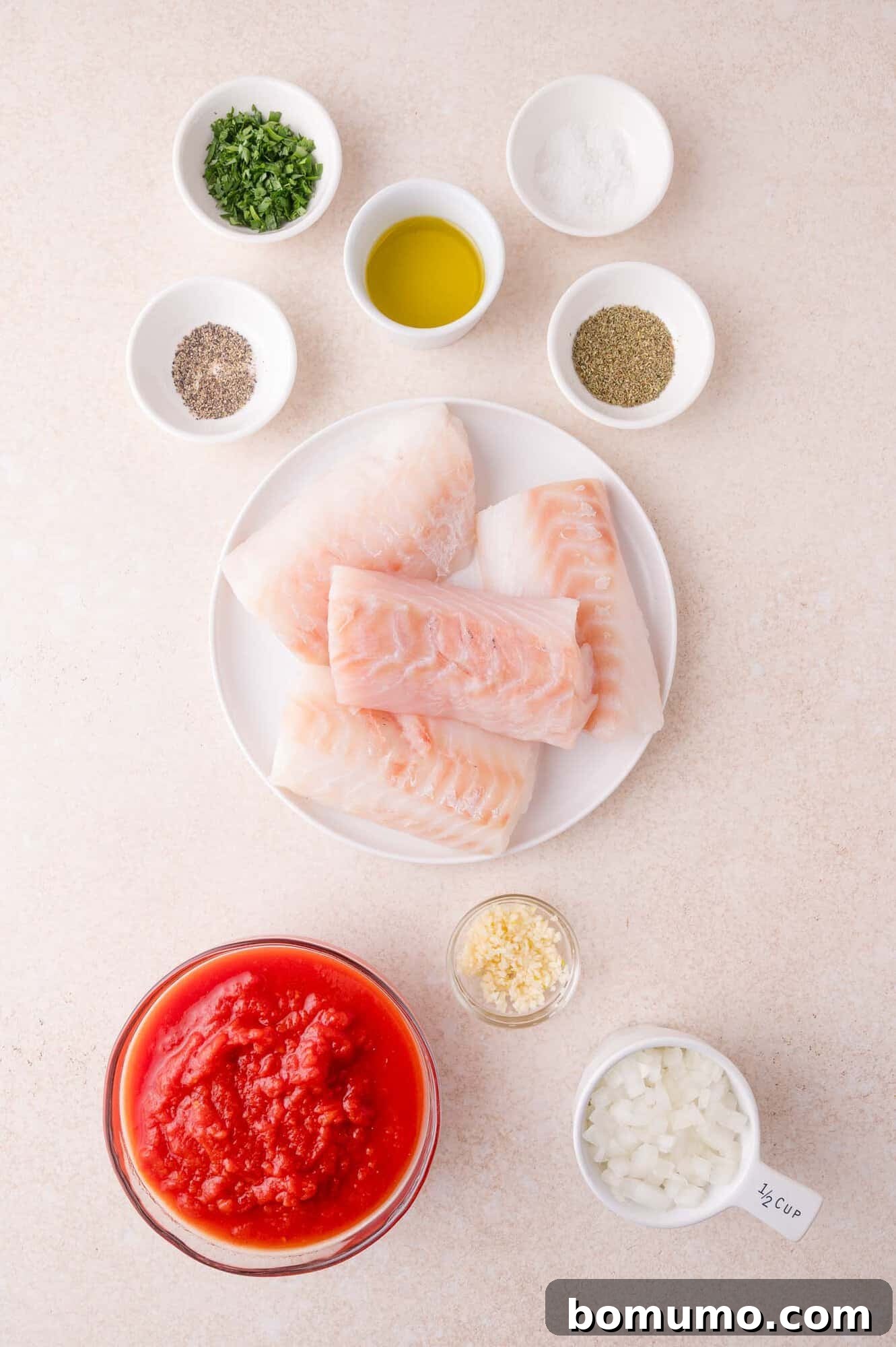 Raw cod fillets on a plate, surrounded by bowls of chopped herbs, olive oil, salt, pepper, Italian seasoning, minced garlic, chopped onion, and crushed tomatoes.
