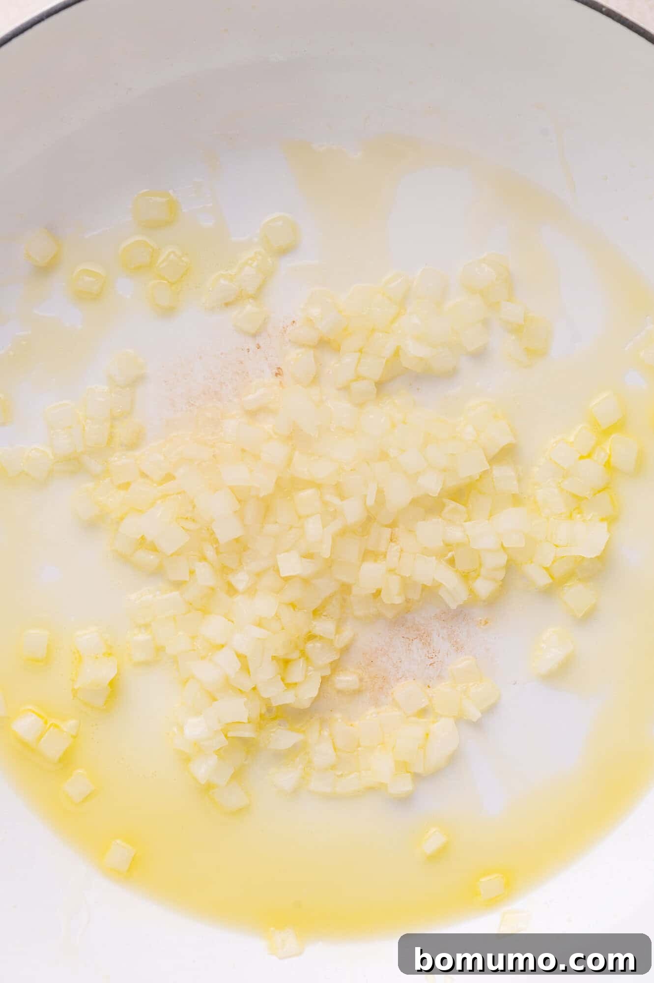Diced onions cooking in oil in a white pan.