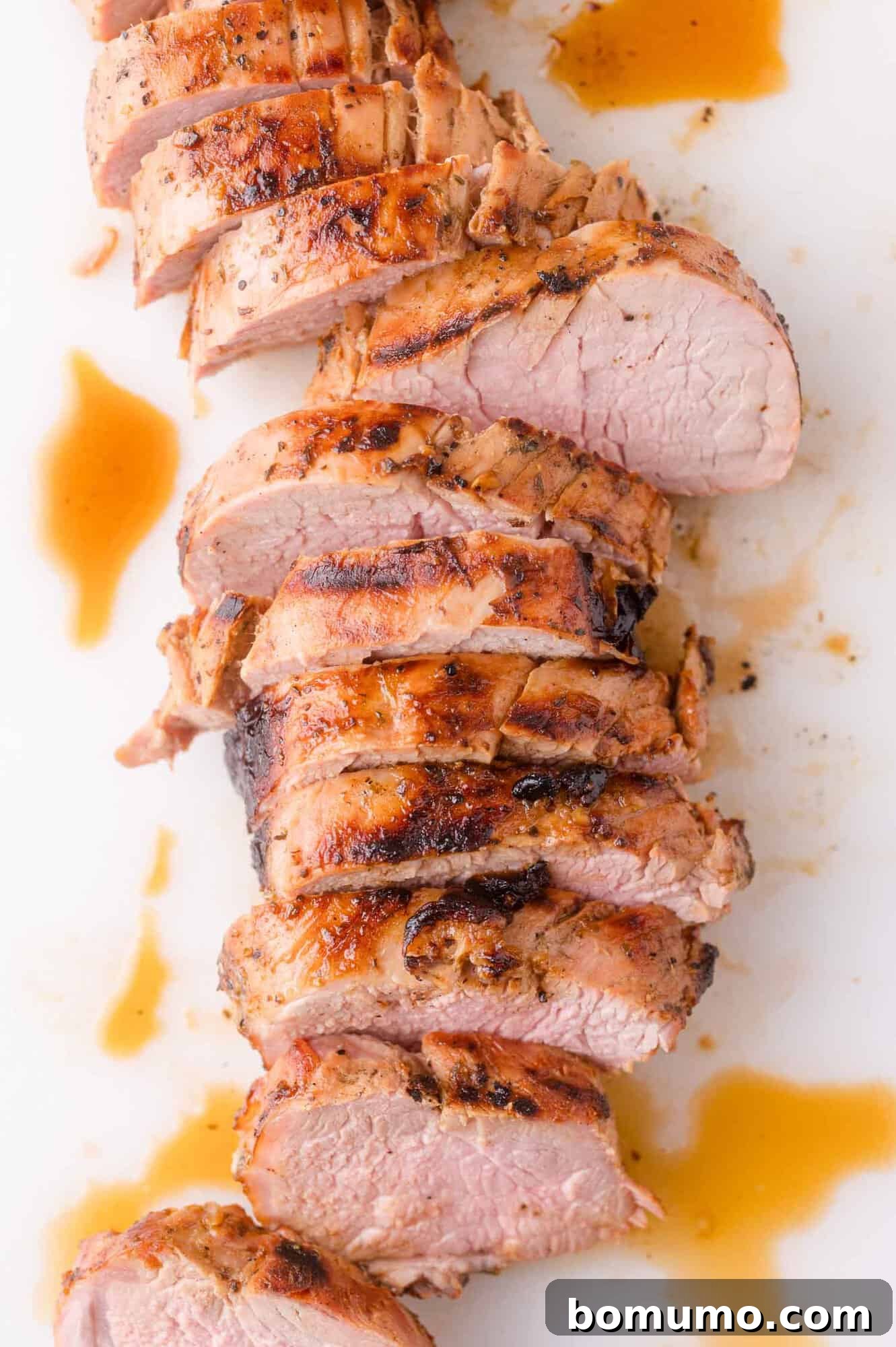 Sliced cooked pork tenderloin with grill marks, arranged on a white surface with a drizzle of brown sauce.