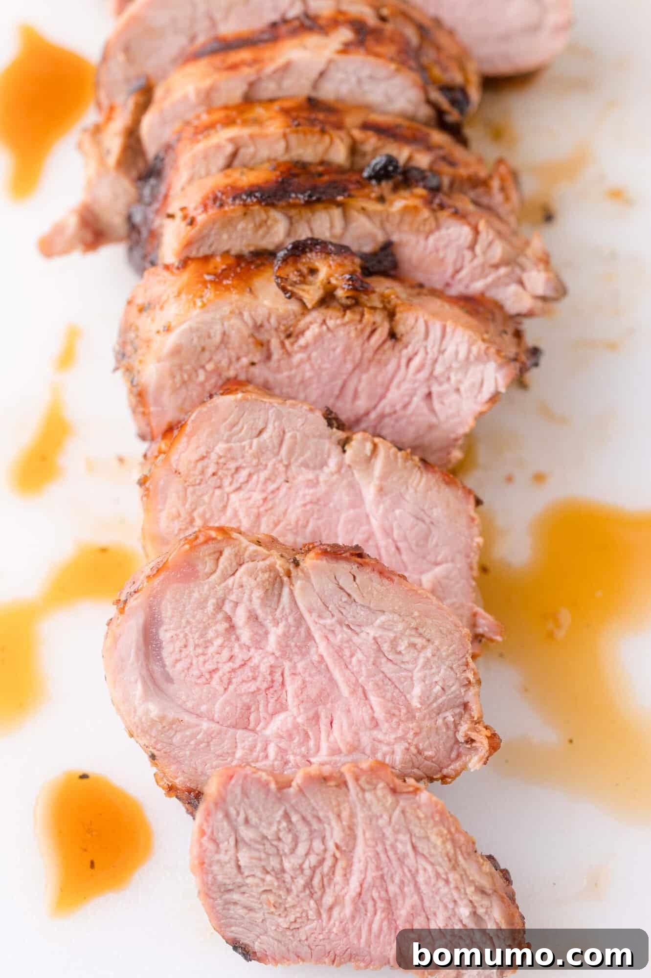 Sliced cooked pork tenderloin arranged in a row on a white surface with juices around the meat.