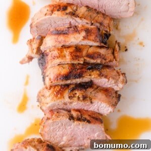Sliced roasted pork tenderloin with a browned, seasoned crust and juices on a white surface.