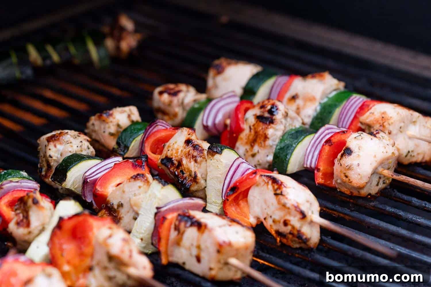 Chicken and vegetable skewers, including zucchini, red onion, and red bell pepper, cooking on a grill.