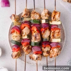 Four grilled chicken and vegetable kabobs with pieces of chicken, red onion, zucchini, and red bell pepper arranged on a round plate.