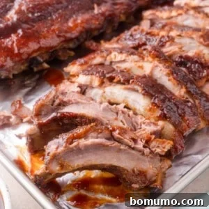 A tray of sliced, cooked barbecue ribs with a glossy, saucy coating, displayed on a metal baking sheet.