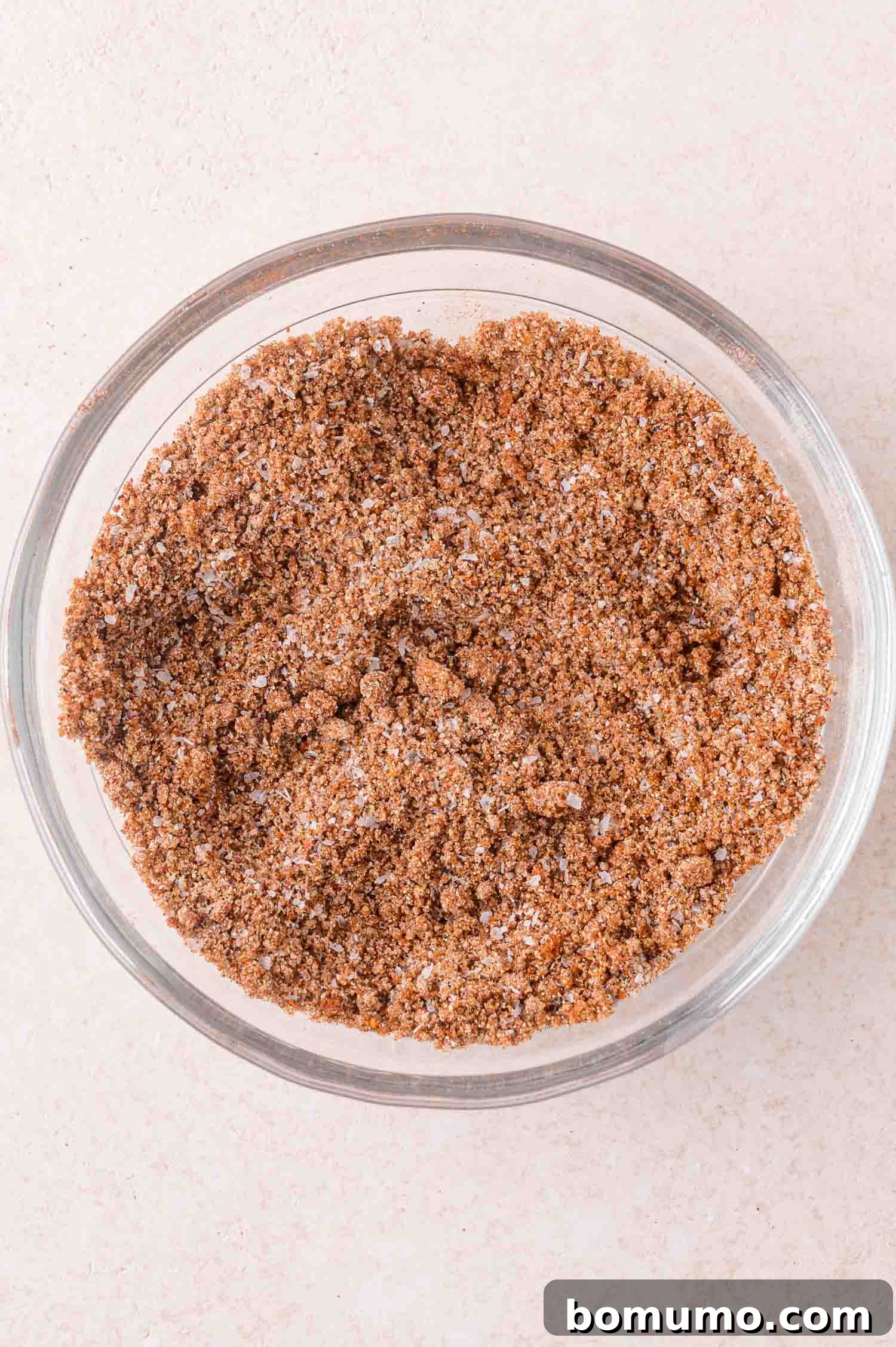 A clear glass bowl filled with a mixture of brown and white dry seasoning or spice blend, placed on a light-colored surface.