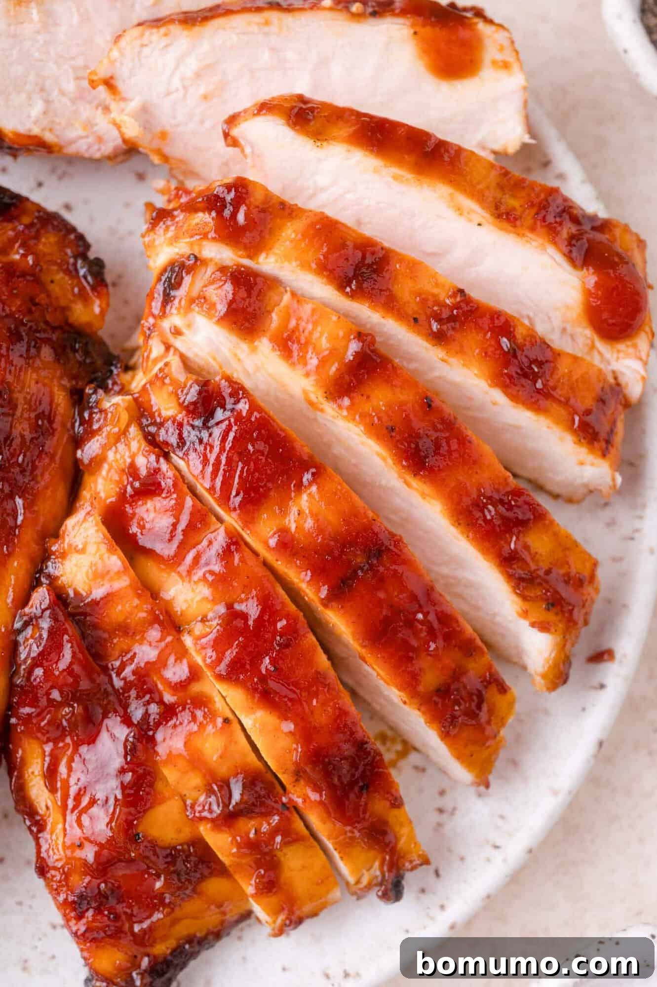 Sliced grilled chicken breast with a reddish-brown barbecue sauce arranged on a white plate.