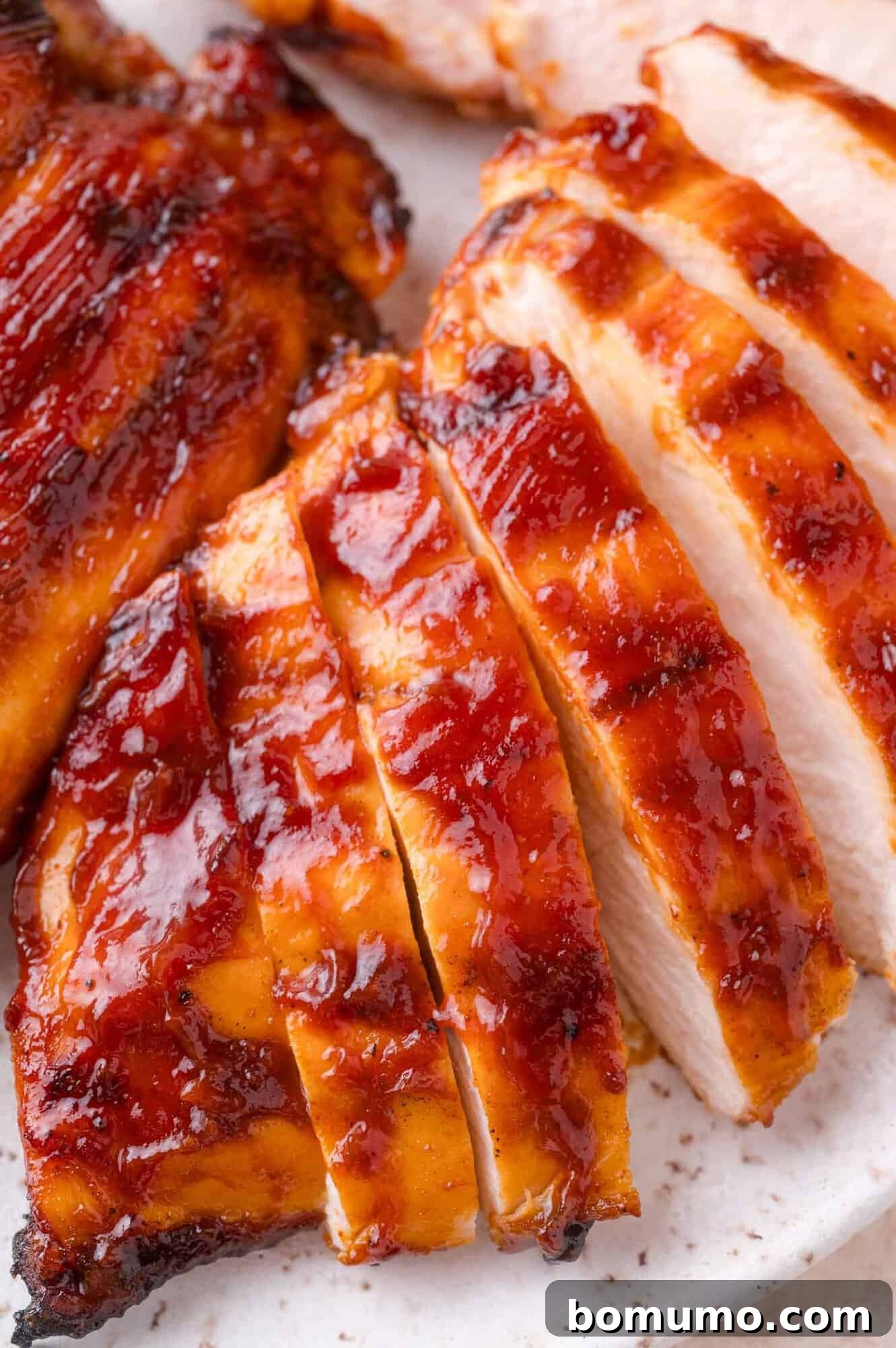Sliced, glazed barbecue chicken breast arranged on a white plate, showing a caramelized, glossy surface.