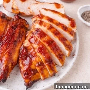 Sliced grilled chicken breast coated in barbecue sauce on a white plate, with small bowls of pepper and salt nearby.