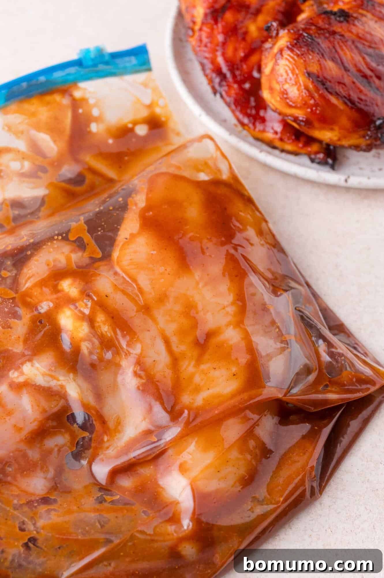 Raw chicken breasts marinating in a sealed plastic bag with sauce, next to a plate of cooked, glazed chicken.