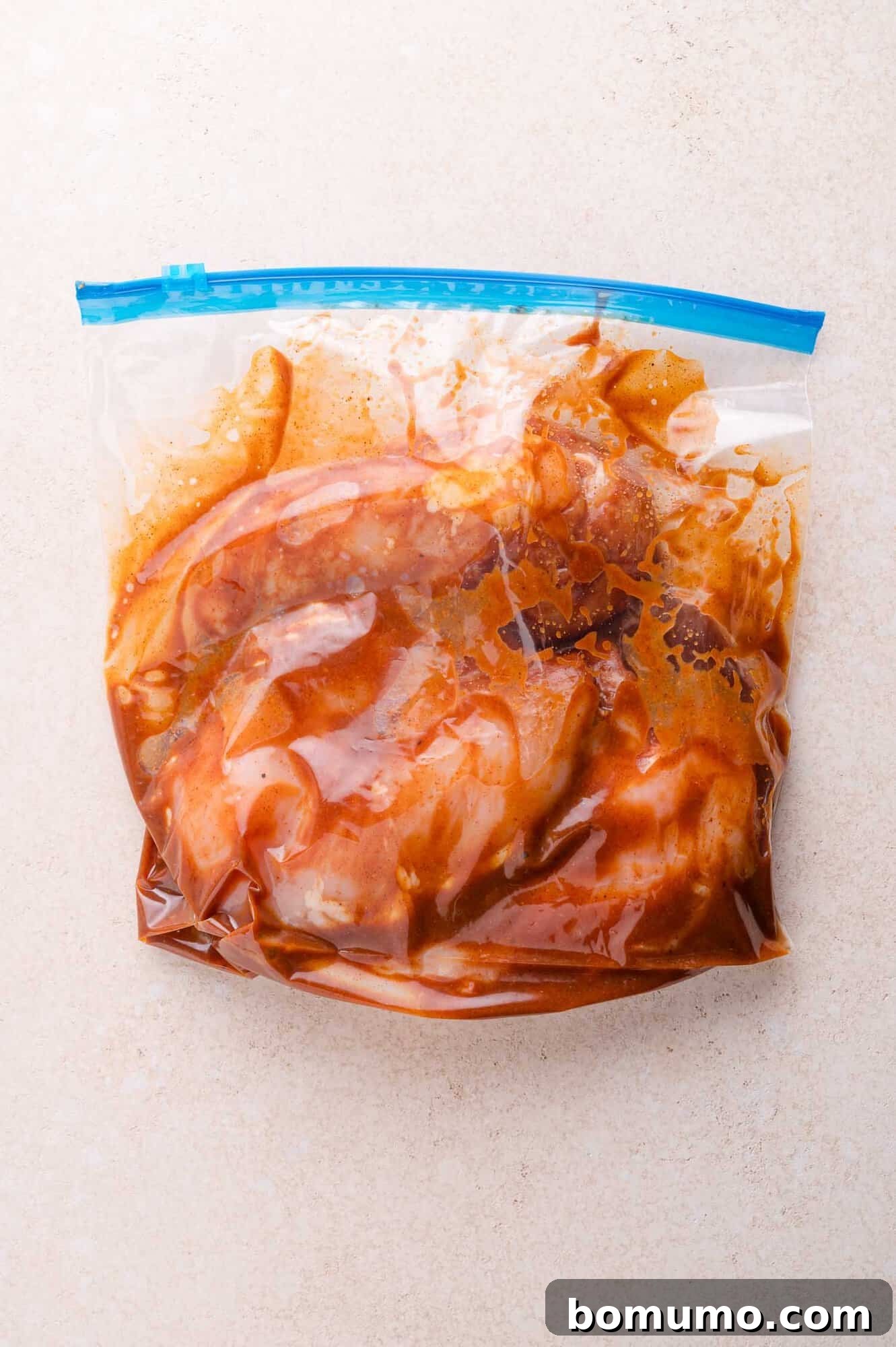 A resealable plastic bag containing raw meat marinating in a bbq marinade on a light-colored surface.
