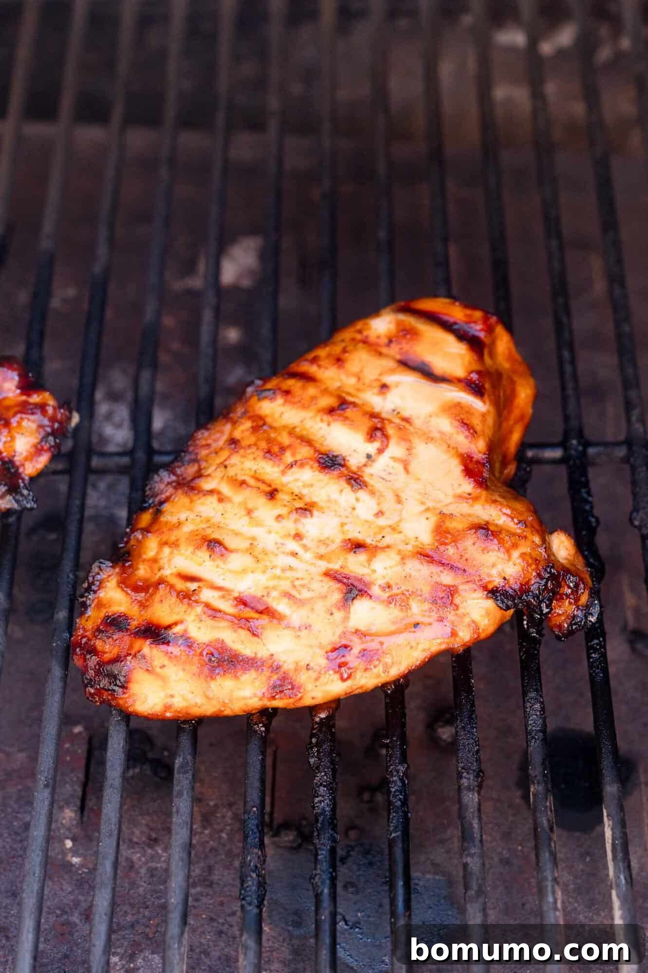 A grilled chicken breast with visible char marks cooking on a barbecue grill.