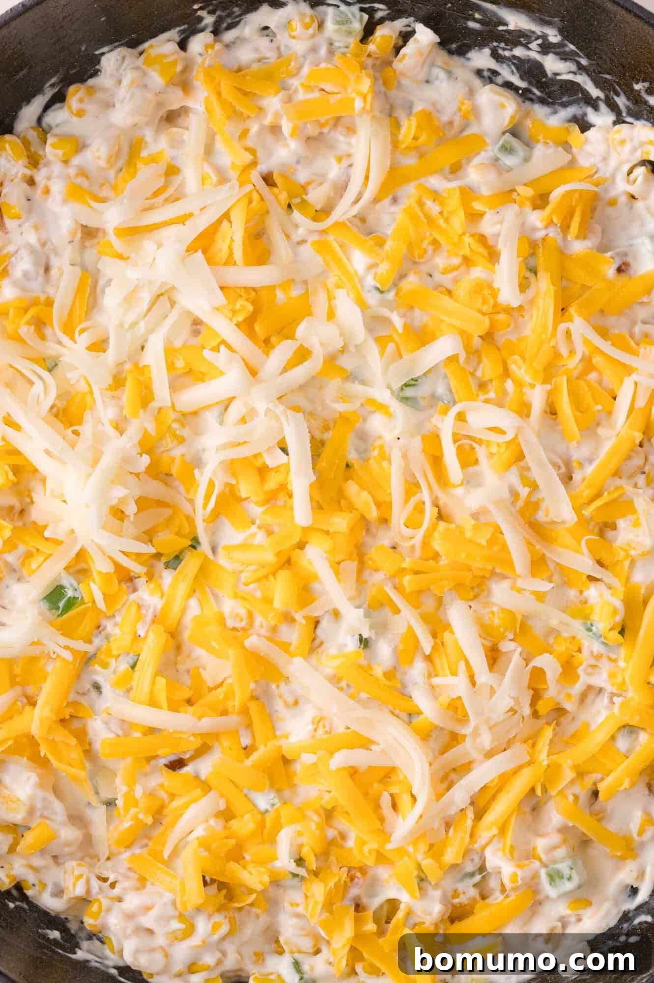 A close-up of a creamy dip mixture topped with shredded yellow and white cheese in a pan.