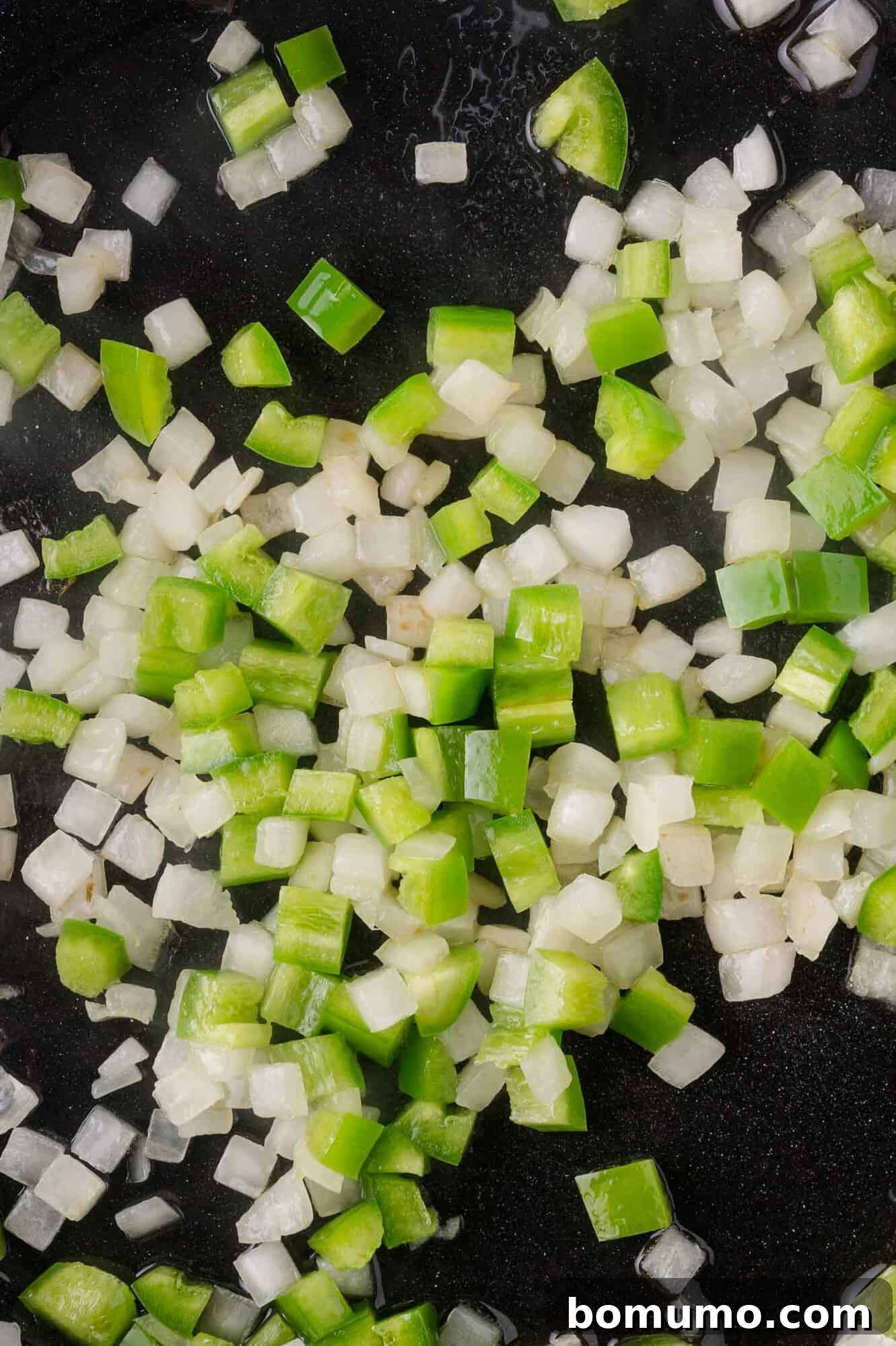 Diced jalapeno peppers and onions cooking in a pan.