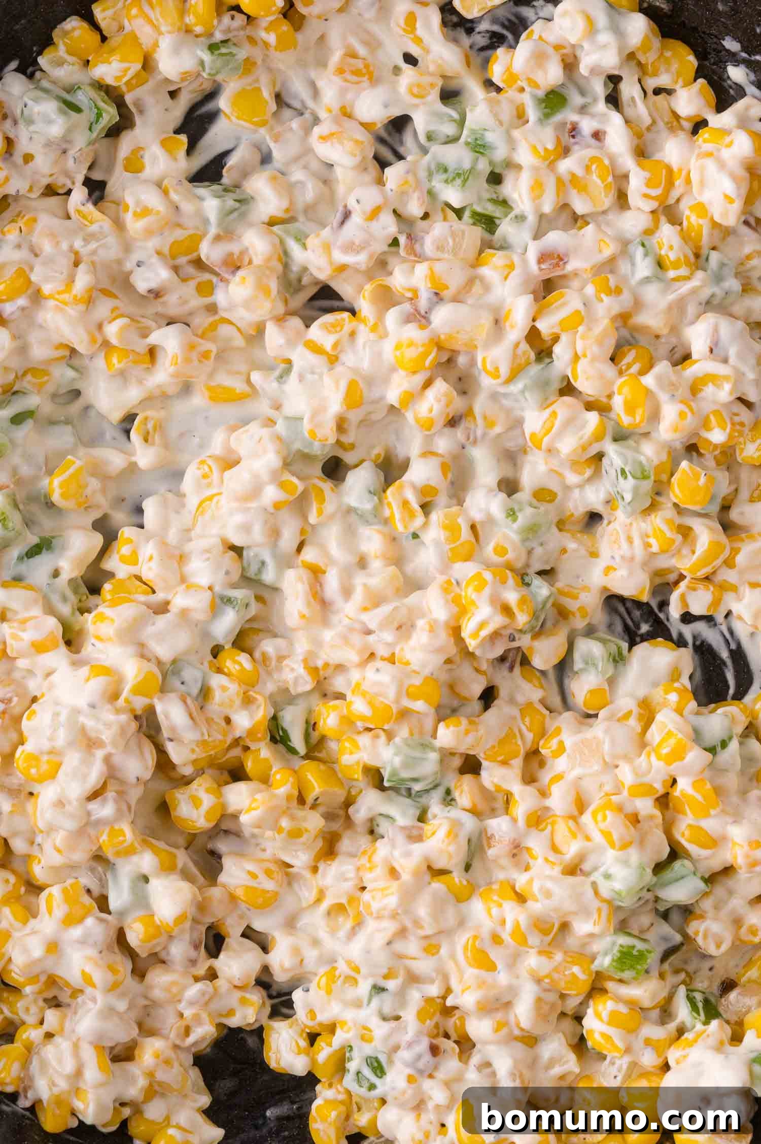 Close-up of creamy corn mixed with diced peppers and onions.