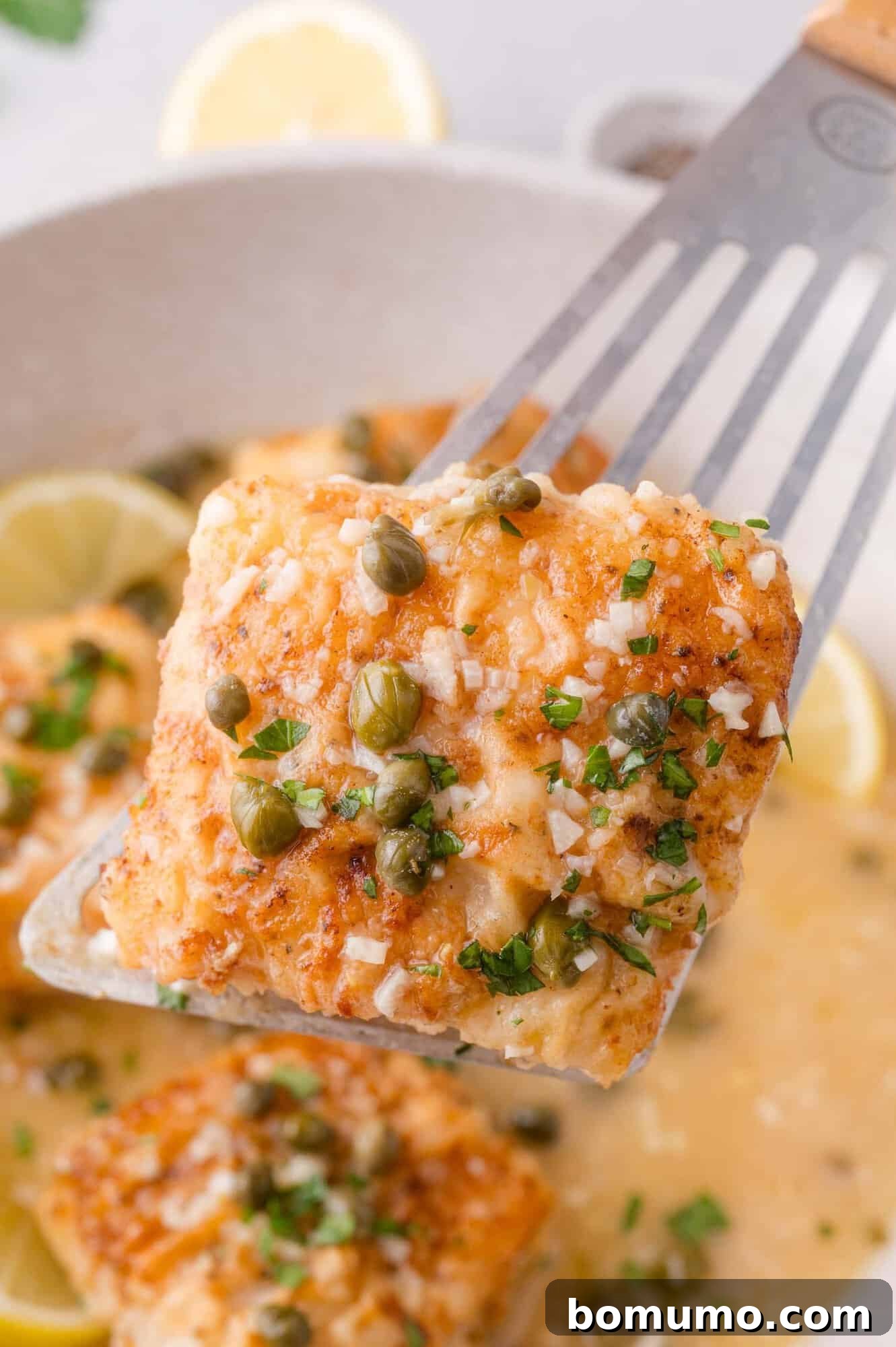 Lemon-Caper Cod Piccata 11 A spatula lifts a piece of cooked cod piccata topped with capers and parsley.