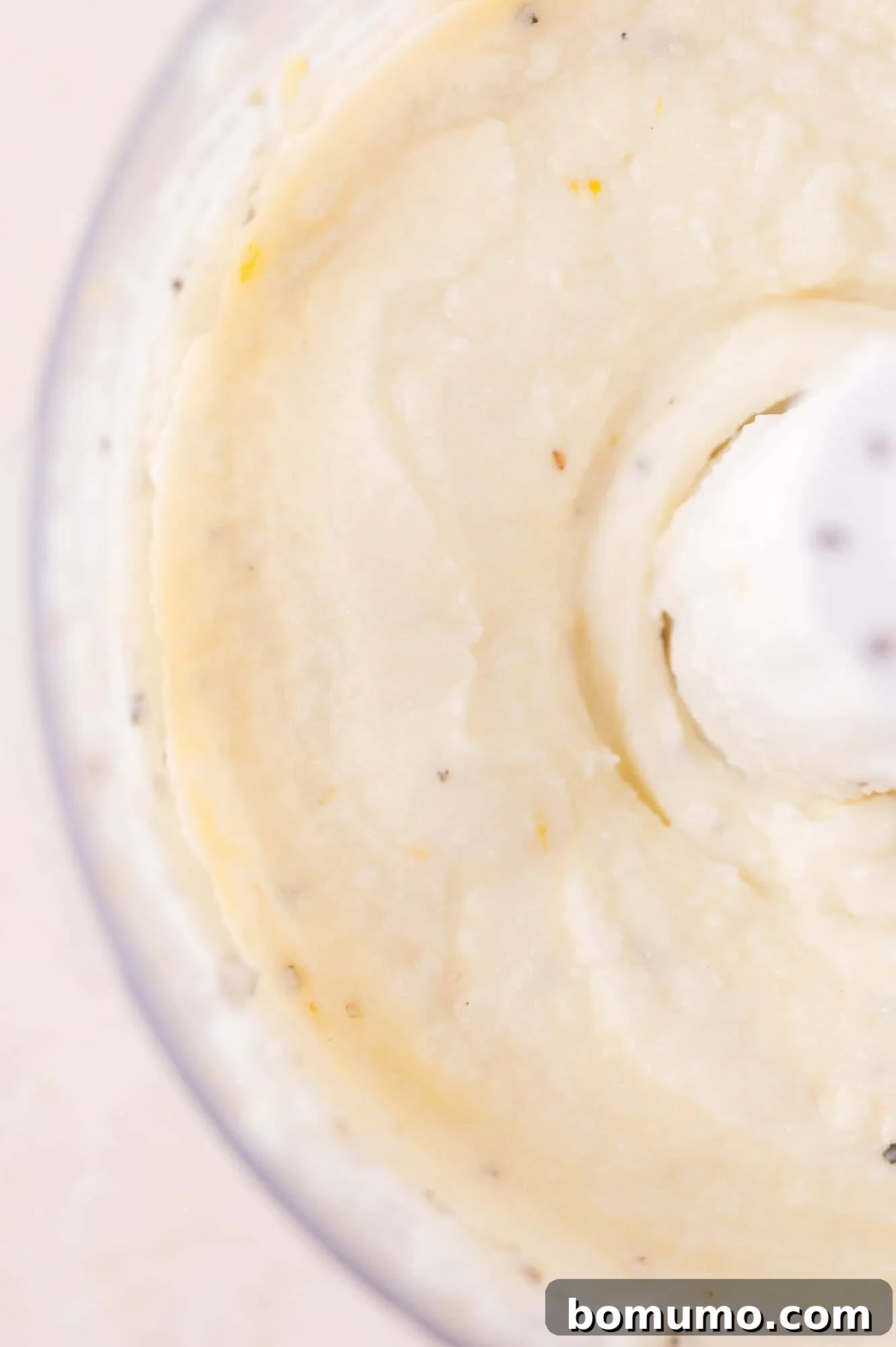 Close-up of smooth, creamy mixture being blended in a food processor, with visible flecks of seasoning throughout.