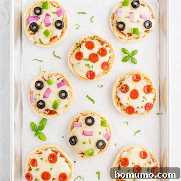 Overhead view of english muffin pizzas on a parchment paper lined baking sheet.