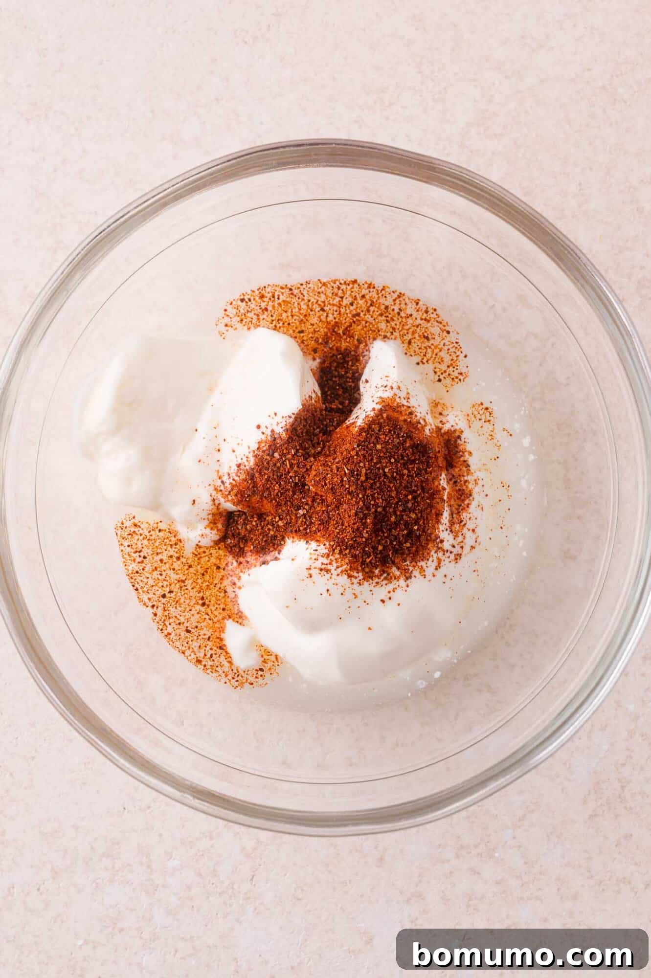 A clear glass bowl contains sour cream, chili powder, and lime juice.
