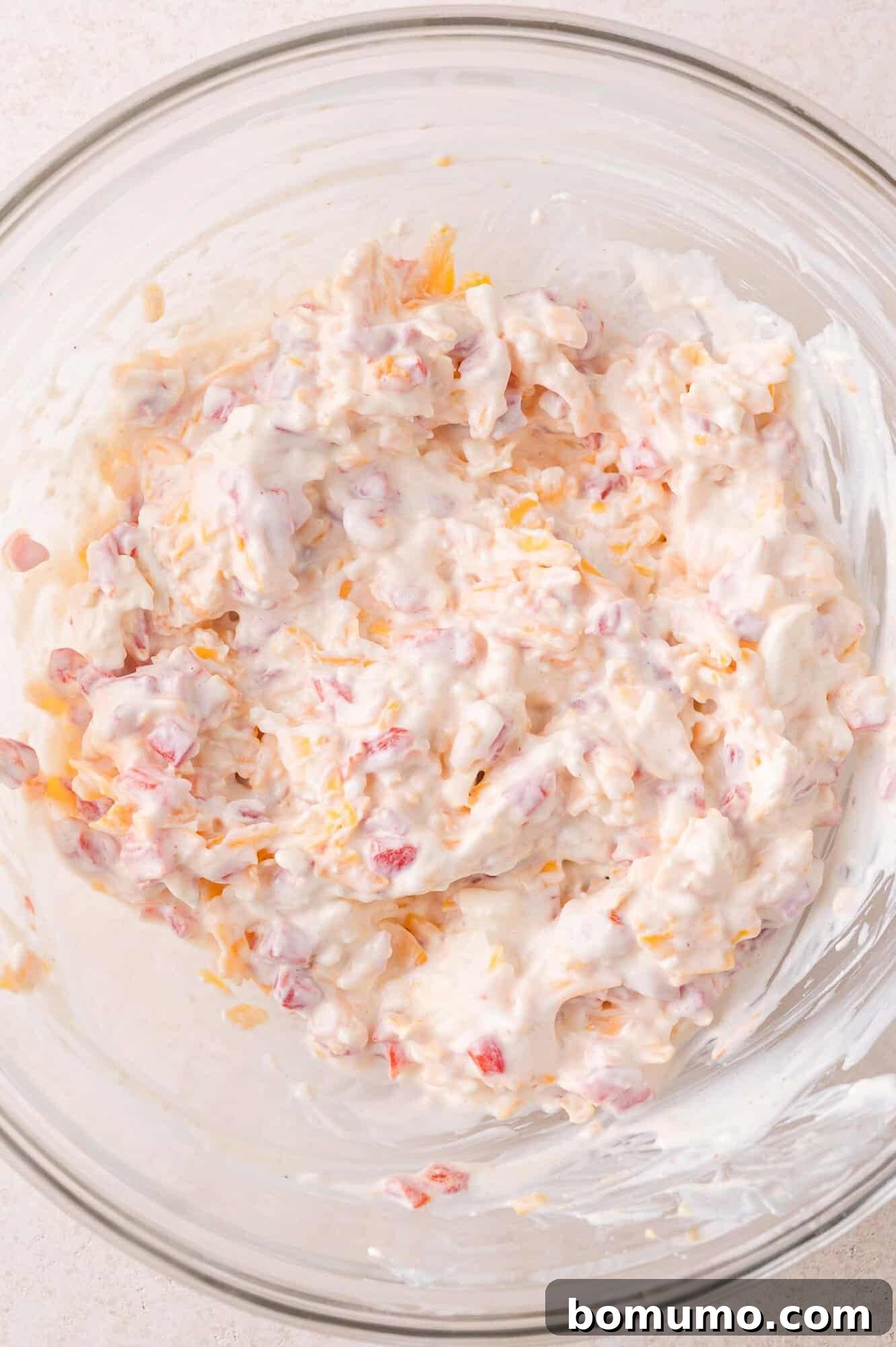 A glass bowl filled with a creamy pimento cheese dip.