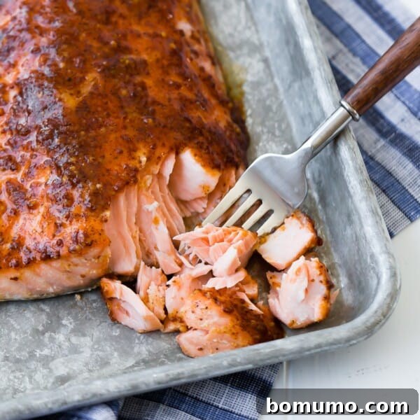 Maple mustard baked salmon on a sheet pan, being flaked with a fork.