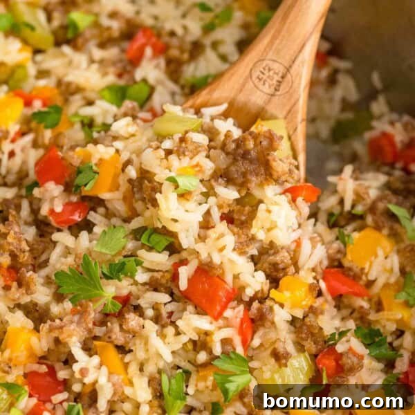 Close up of sausage, rice, and bell peppers in a skillet with a wooden spoon.