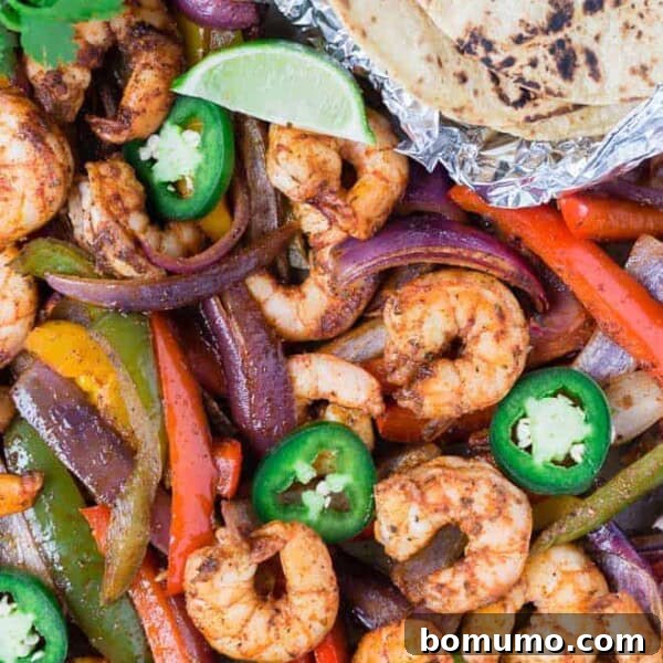 Colorful shrimp fajitas on a sheet pan with tortillas, limes, jalapeno, and cilantro.