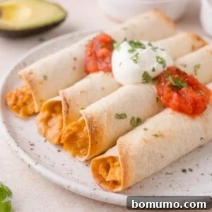 Four baked taquitos filled with a creamy mixture, topped with salsa, sour cream, and chopped herbs, served on a white plate with a sliced avocado in the background.