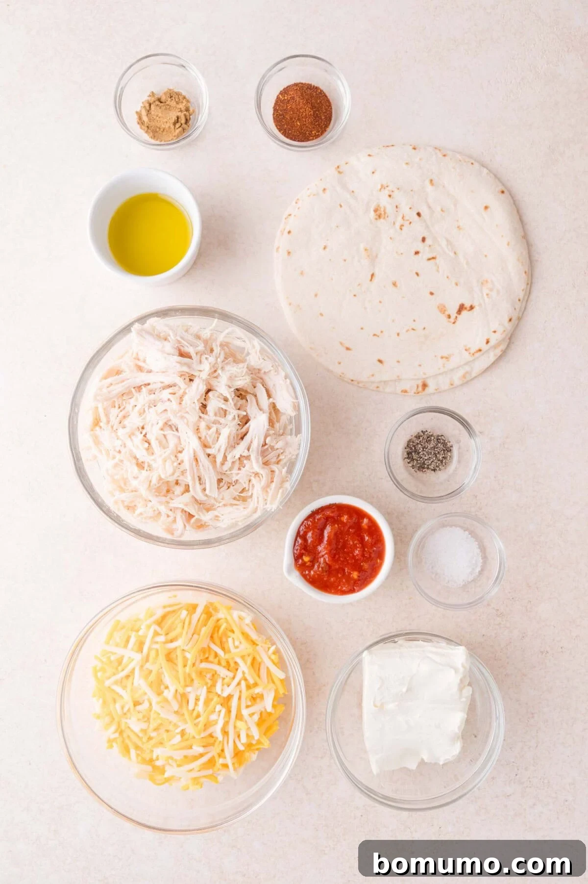 Ingredients for a baked taquitos arranged on a white surface, including shredded chicken, shredded cheese, cream cheese, salsa, tortilla, spices, olive oil, salt, and pepper.