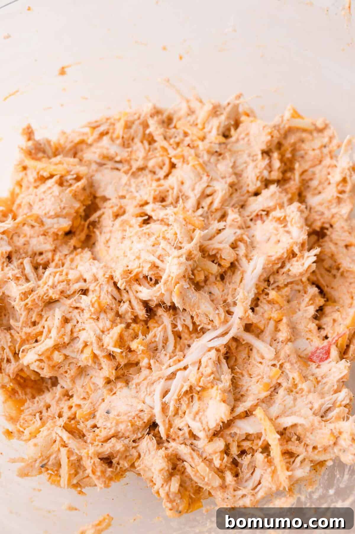 Shredded chicken mixed with spices and a creamy sauce in a clear glass bowl.