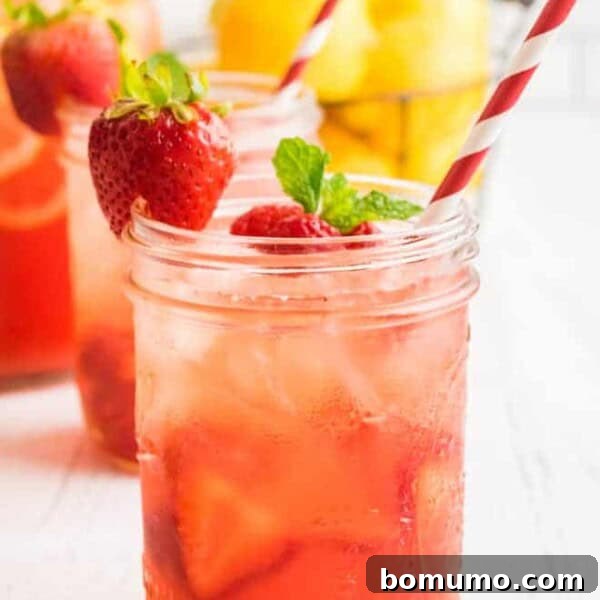 Sparkling berry pink lemonade in a mason jar with a red and white straw. Garnished with a strawberry and fresh mint.