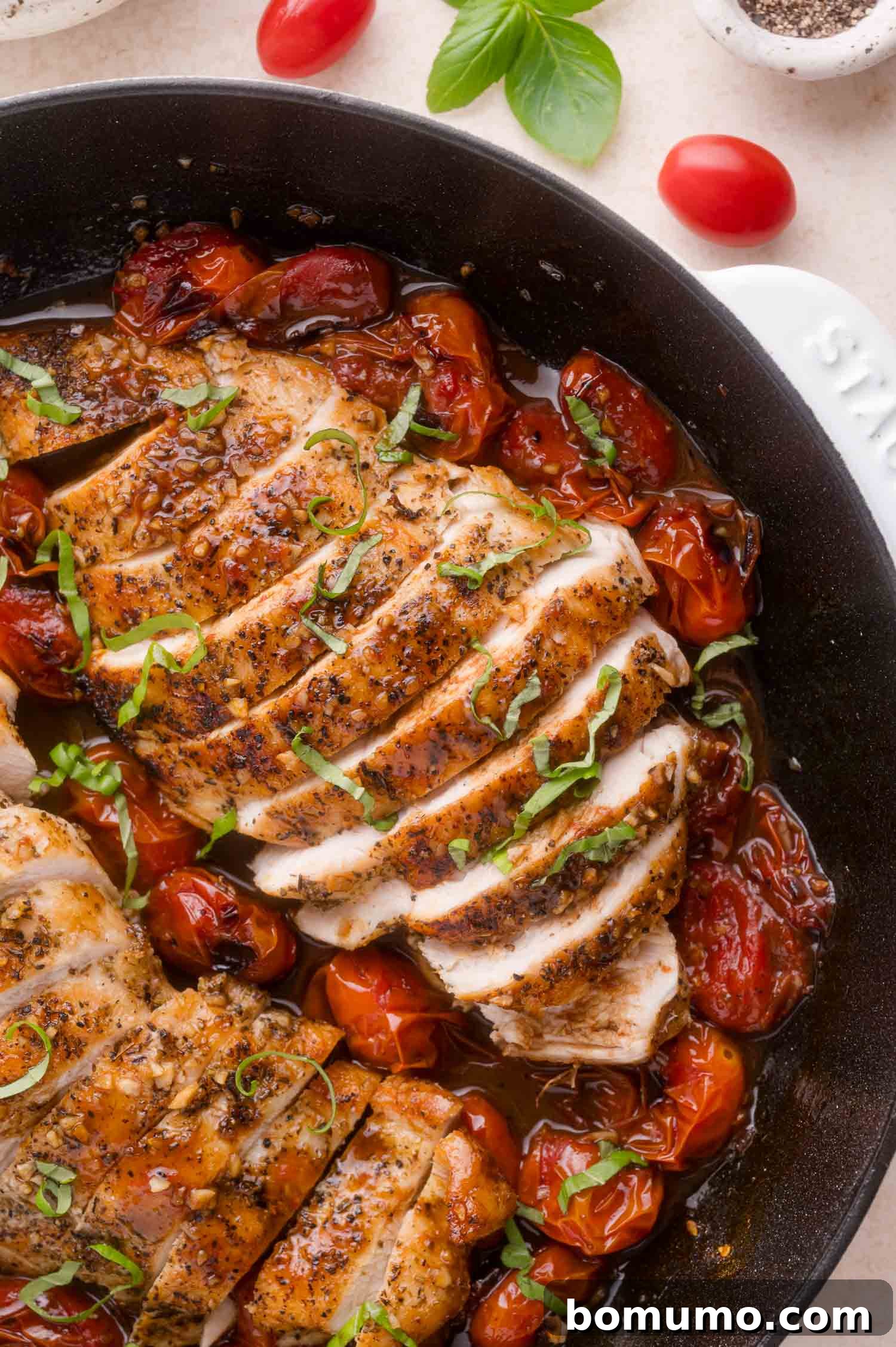 Sliced seasoned chicken breast in a skillet with roasted cherry tomatoes and fresh basil garnish.