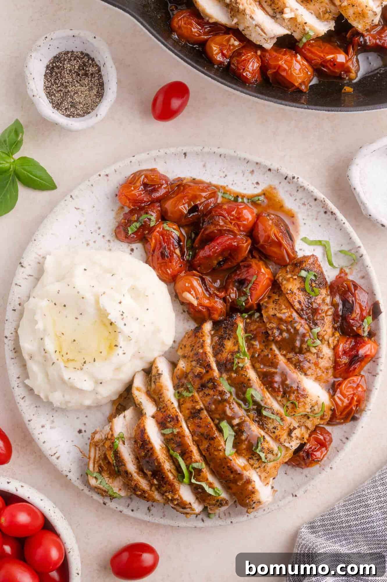 Sliced seasoned chicken breast with roasted cherry tomatoes and a serving of mashed potatoes on a white plate, garnished with fresh herbs.