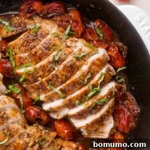 Sliced, seasoned chicken breast in a skillet with roasted cherry tomatoes and fresh basil garnish.