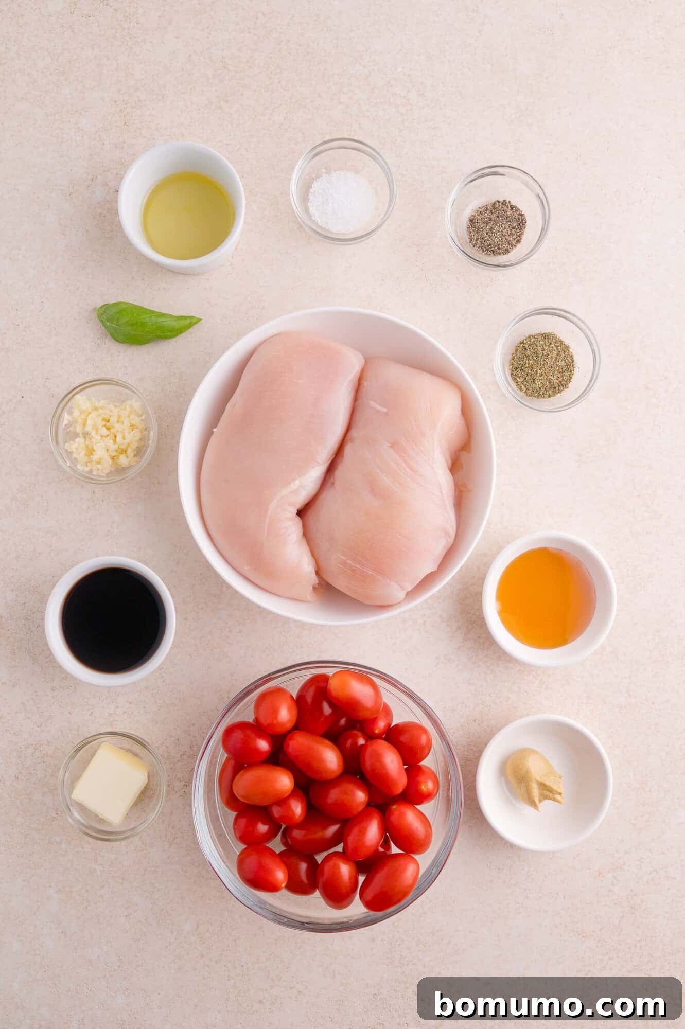 Two raw chicken breasts in a bowl, grape tomatoes in another bowl, and small dishes of oil, salt, pepper, garlic, vinegar, honey, butter, and mustard arranged on a light surface.