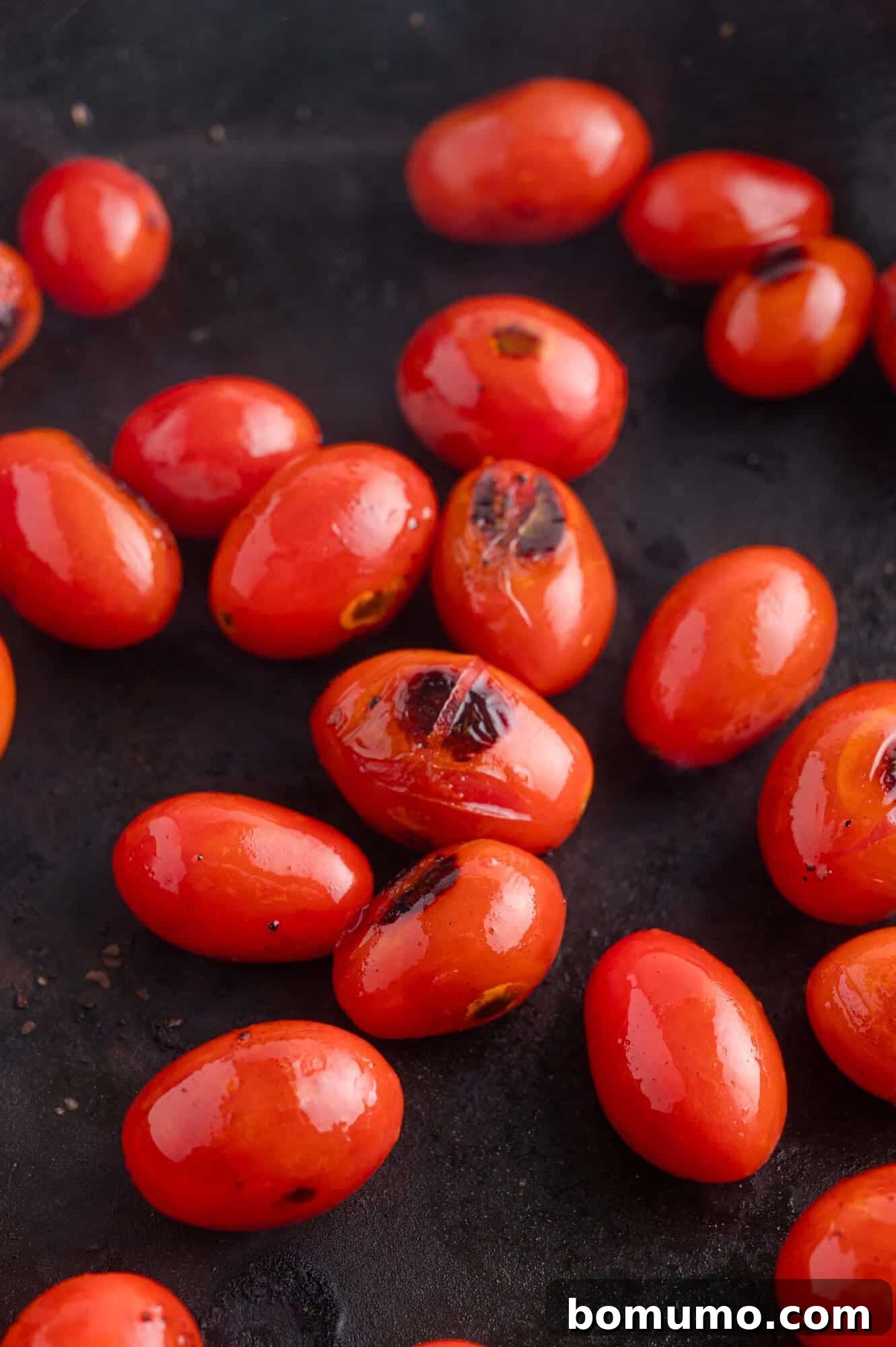 Several roasted grape tomatoes with charred spots are scattered on a dark surface.