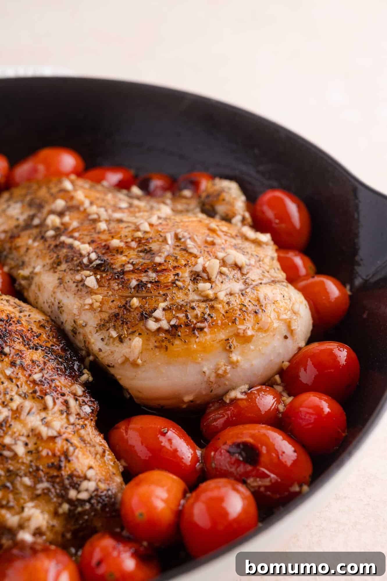 Seasoned chicken breast and cherry tomatoes in a black skillet.