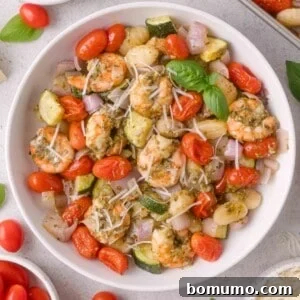 White bowl filled with gnocchi, shrimp, cherry tomatoes, zucchini, red onion, shredded cheese, and basil leaves.