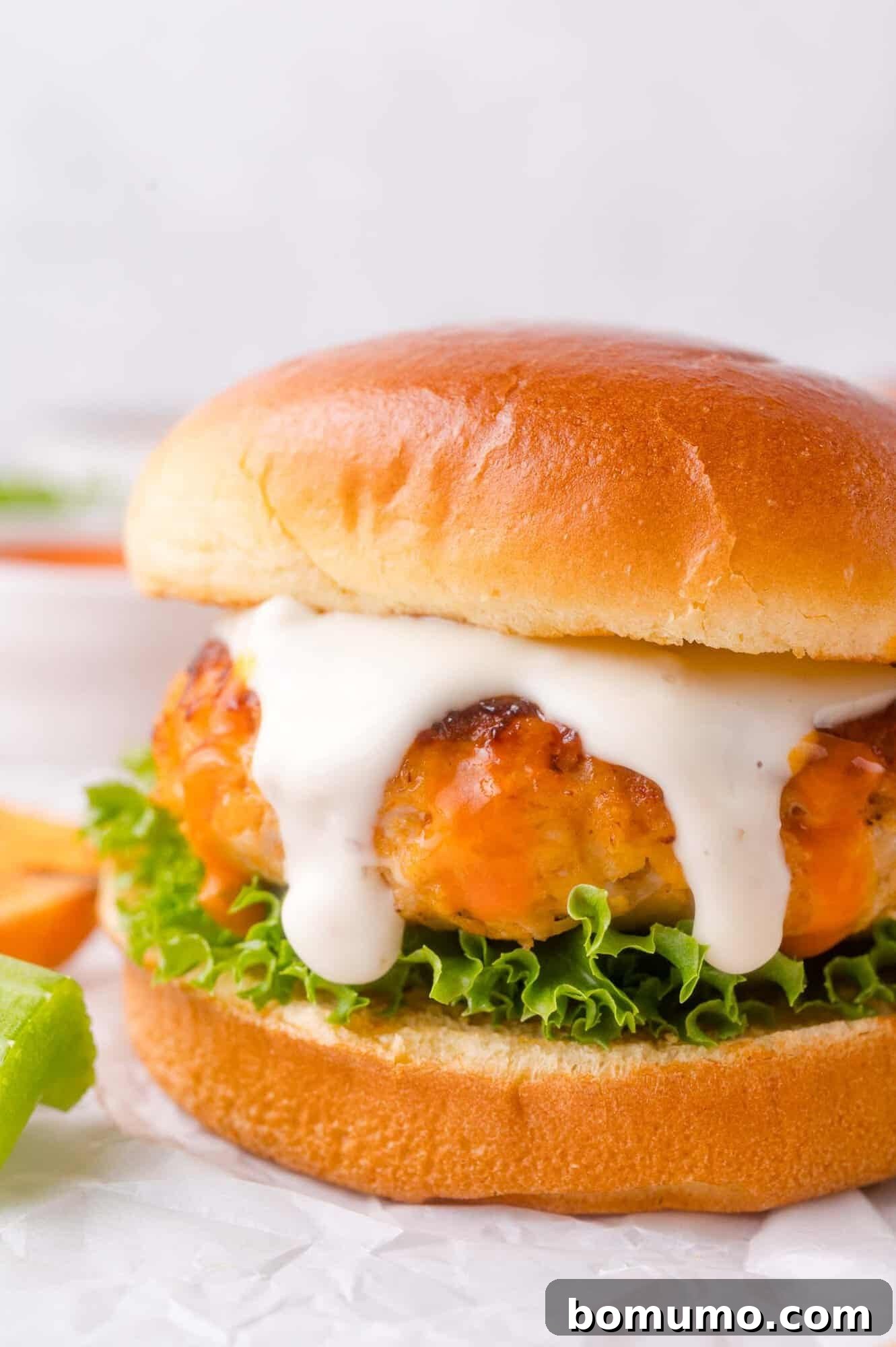 Buffalo chicken burger with lettuce and a thick layer of ranch on a soft bun, shown close up on a piece of parchment paper.