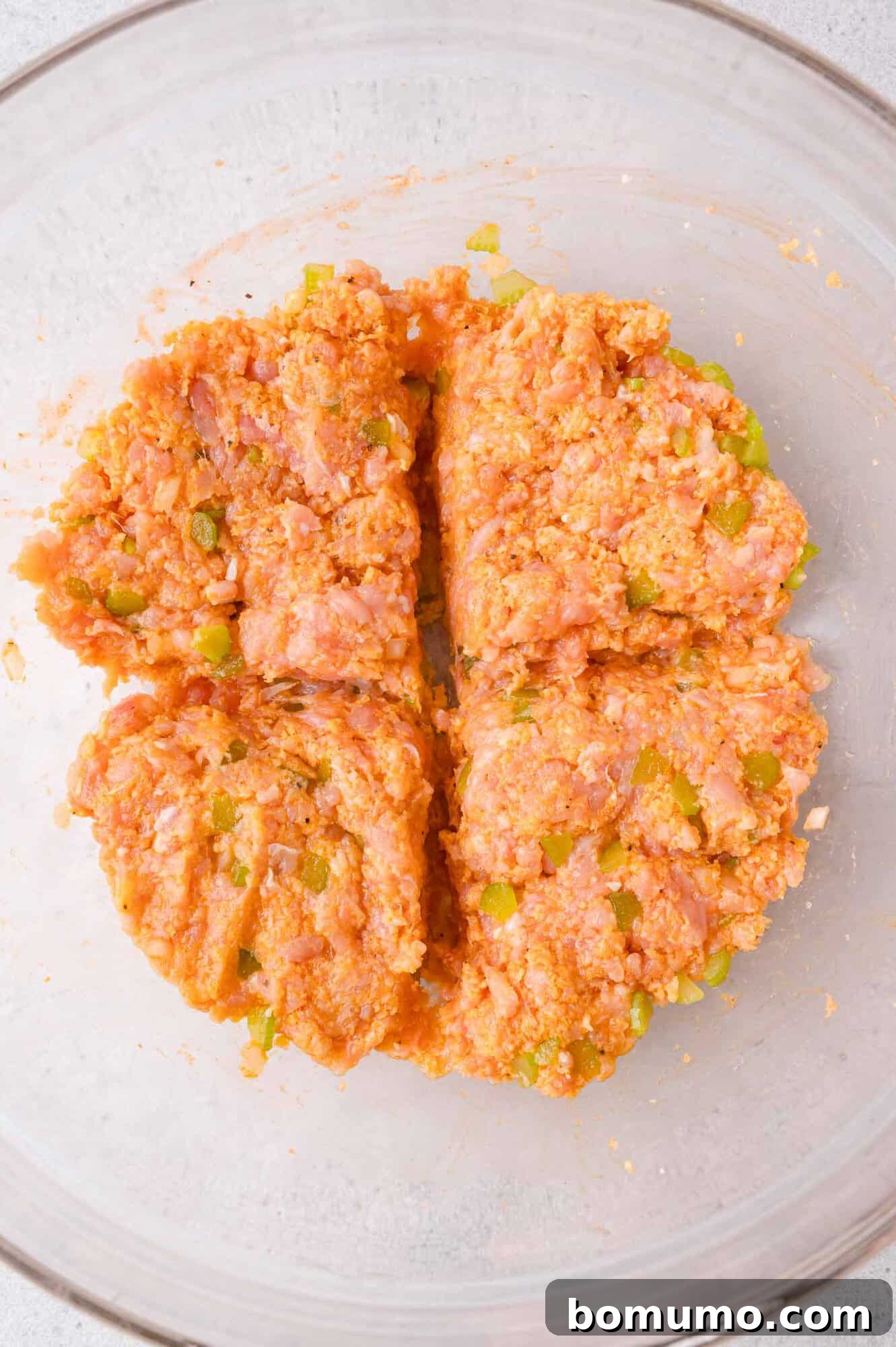Ground chicken mixture with celery in a glass bowl, divided into four equal sections.