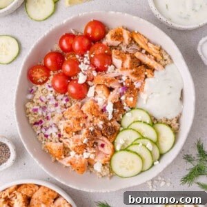 Bowl with quinoa, grilled salmon, cherry tomatoes, cucumbers, diced red onion, feta cheese, and tzatziki sauce.