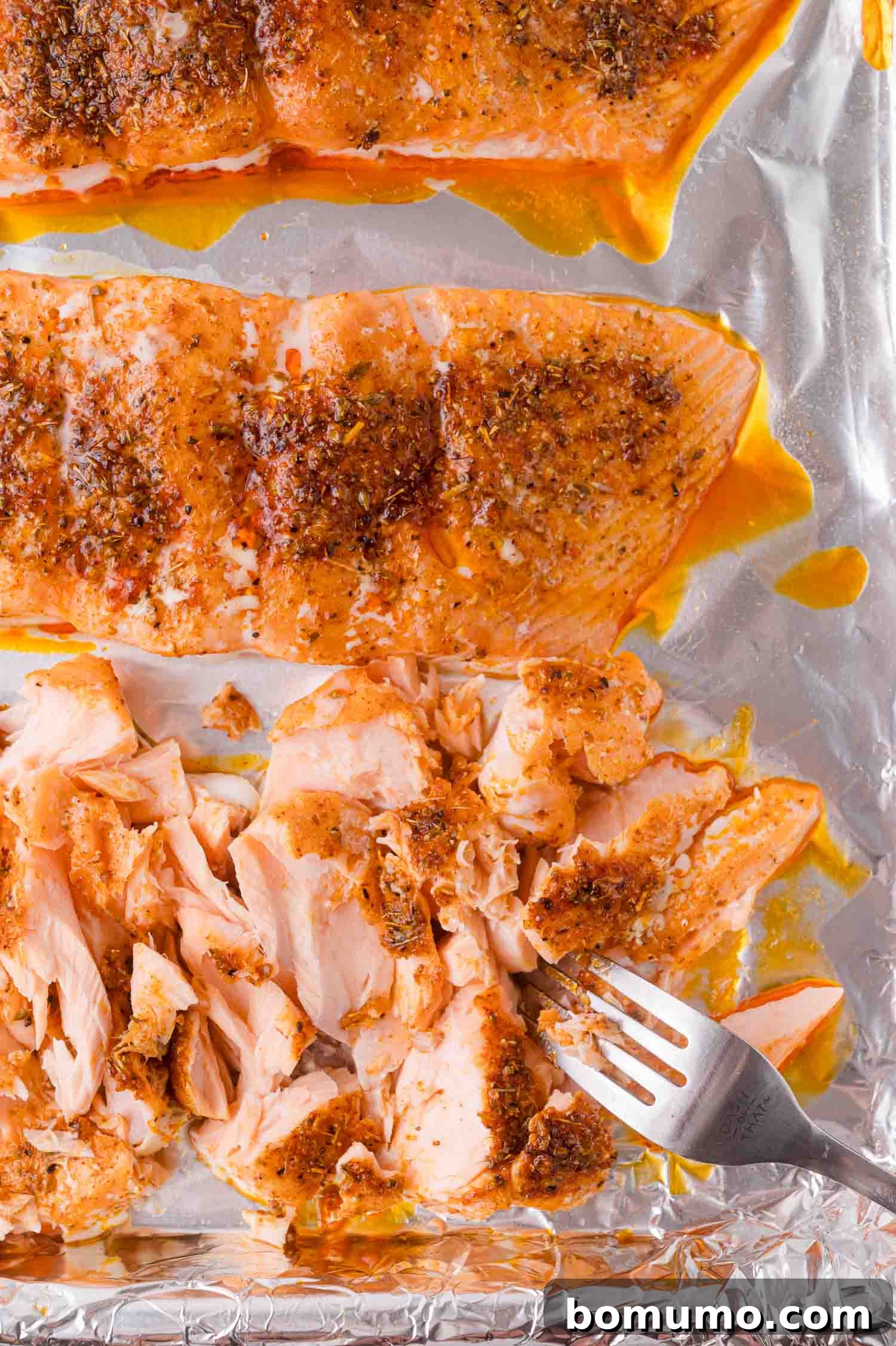 Two baked salmon fillets on foil, one fillet partially flaked with a fork.