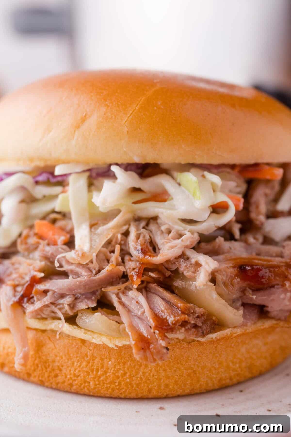 Slow Cooker Apple Cider Pulled Pork Sandwiches 11 Pulled pork sandwich topped with coleslaw on a soft hamburger bun, served on a white plate.