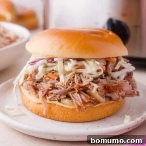 Slow Cooker Apple Cider Pulled Pork Sandwiches 17 Pulled pork sandwich topped with coleslaw on a white plate.