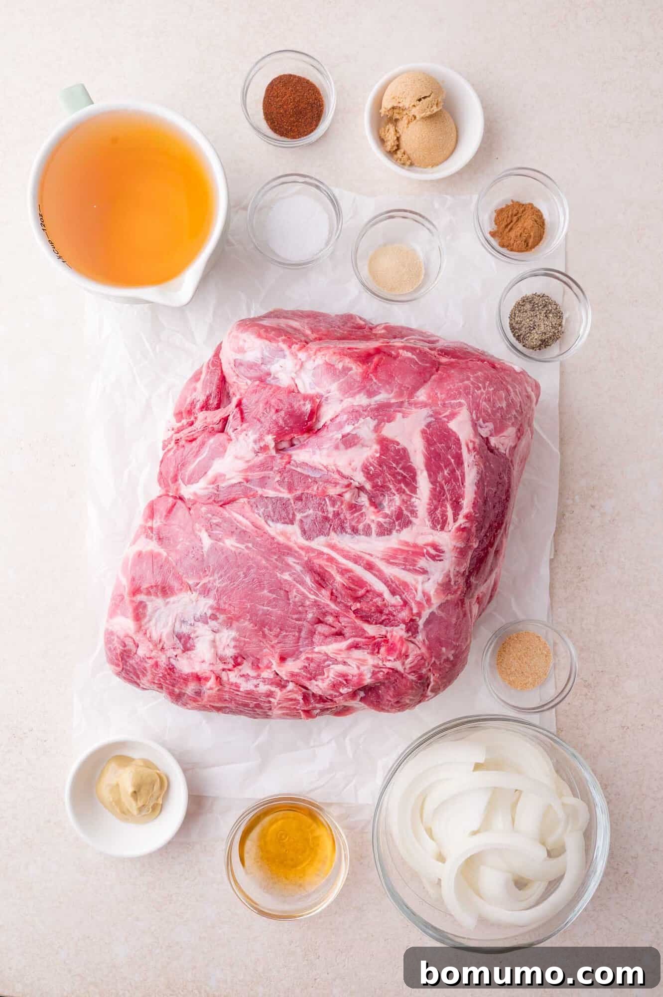 Slow Cooker Apple Cider Pulled Pork Sandwiches 4 A raw pork shoulder on parchment paper is surrounded by small bowls of seasonings, sliced onions, broth, mustard, and brown sugar on a light surface.