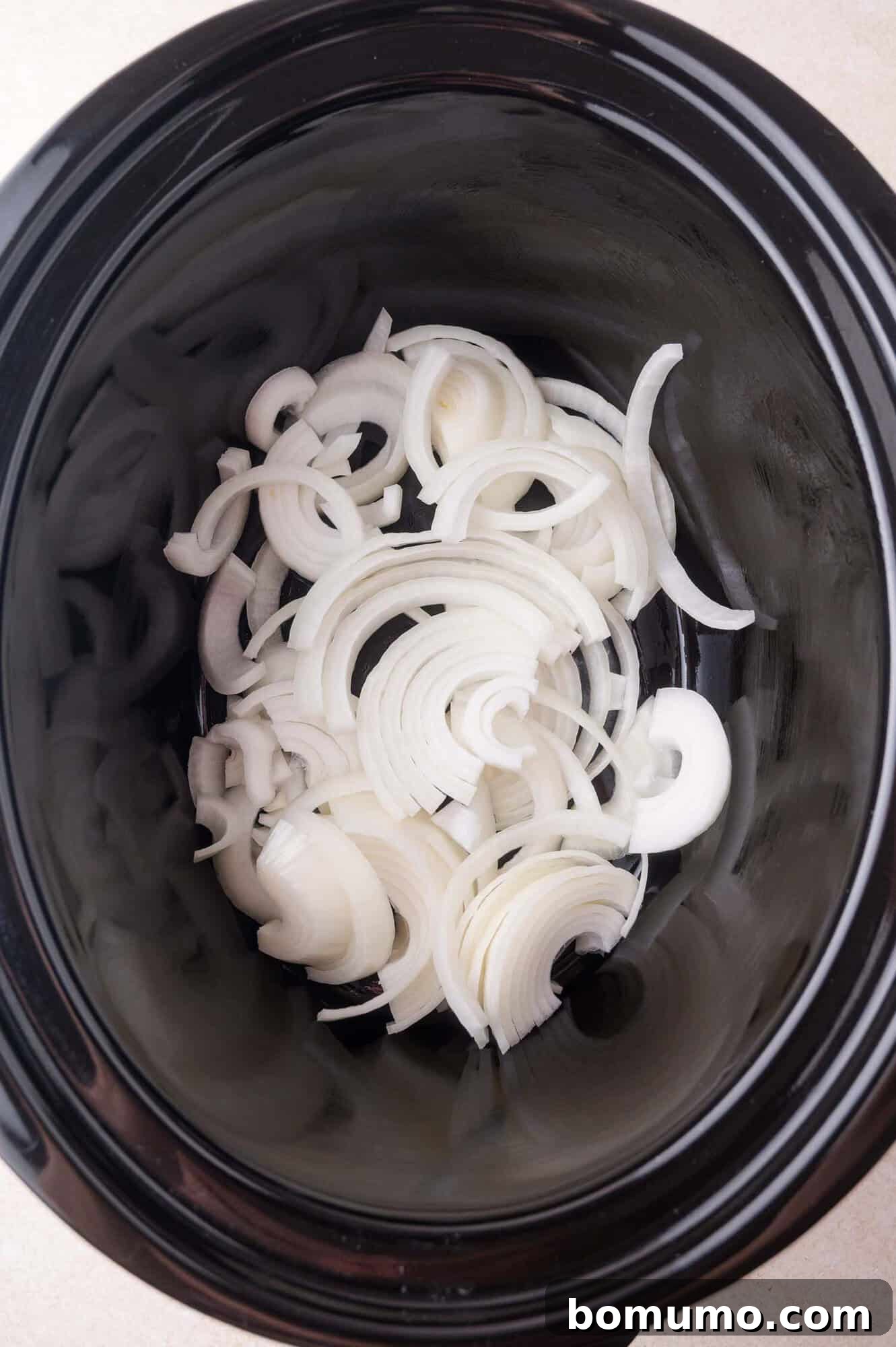 Slow Cooker Apple Cider Pulled Pork Sandwiches 5 Sliced white onions spread at the bottom of a black slow cooker.